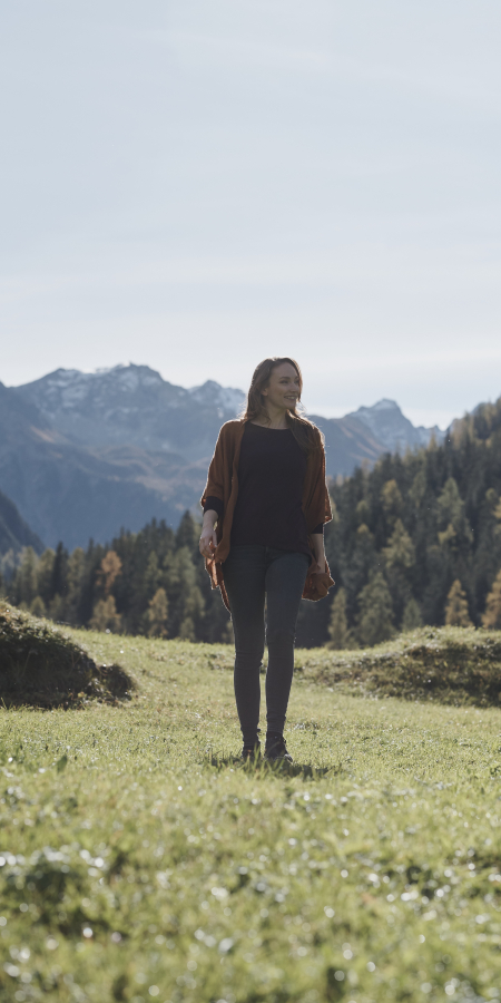 Bergluft und Freiheit – Ferien für Alleinreisende in Graubünden (Foto: © Samuel Trümpy) Ferien für Alleinreisende: Frau steht alleine auf einer Wiese vor alpiner Bergkulisse in Graubünden
