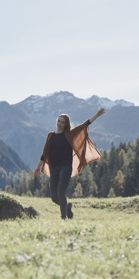 Bergluft und Freiheit – Ferien für Alleinreisende in Graubünden (Foto: © Samuel Trümpy) Ferien für Alleinreisende: Frau steht alleine auf einer Wiese vor alpiner Bergkulisse in Graubünden