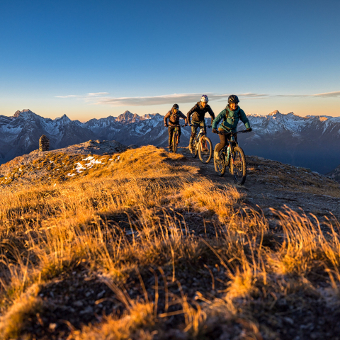 Frühmorgens unterwegs auf den hochgelegenen Trails Graubündens – ideale Bedingungen, um die Bikesaison im Herbst abzuschliessen Mountainbiker bei Sonnenaufgang auf einem Grat im herbstlichen Graubünden