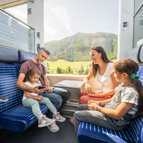 Mit dem TrenInn-Billett wird die Fahrt durch das Engadin zum Erlebnis (Foto: © Marco Hartmann) Eine Familie sitzt in einem Zugabteil der Rhätischen Bahn und schaut auf ein Smartphone