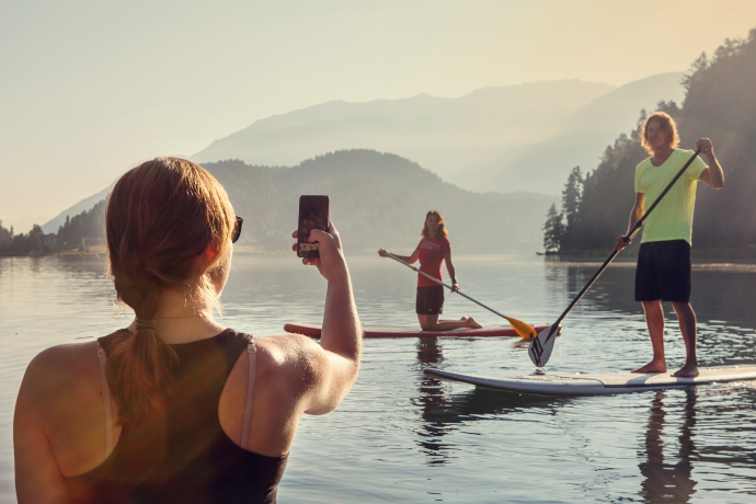 Der St. Moritzersee eignet sich bestens fürs Stand-up-Paddling (Foto: © Engadin Tourismus AG / Filip Zuan) Eine Frau fotografiert mit einem Smartphone einen Mann und eine Frau auf Boards fürs Stand-up-Paddling auf dem St. Moritzersee