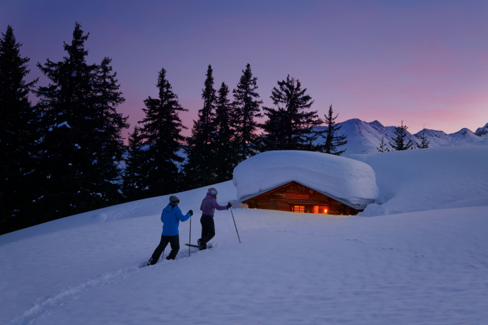 Berghütten und Maiensässe sind beliebte Tourenziele (Foto: © Graubünden Ferien / Stefan Schlumpf) Ein Paar in Schneeschuhen stapft zu einer Berghütte
