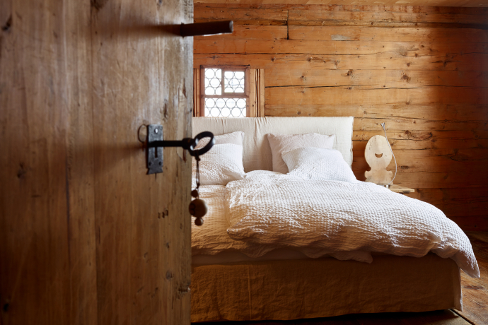 Nühus B&B (Photo: © Graubünden Ferien / Stefan Schlumpf) View through the half-open wooden door of a guest room with a double bed at Nühus B&B