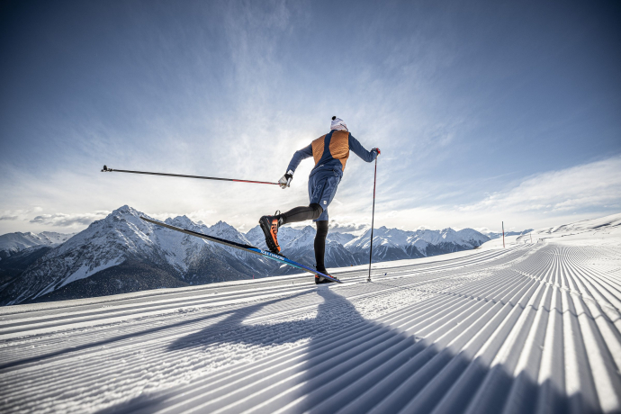 Langlaufen im Unterengadin: Traumhafte Loipen mit beeindruckender Bergkulisse (Foto: © Tourismus Engadin Scuol Samnaun Val Müstair AG (TESSVM) / Andrea Badrutt) Ein Langläufer auf einer verschneiten Loipe im Unterengadin, im Hintergrund ein beeindruckendes Bergpanorama