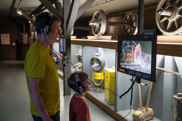 Interaktives Entdecken im Bahnmuseum Albula – Eisenbahngeschichte hautnah erleben in Bergün (Foto: © Rhätische Bahn / Nadine Gall) Vater und Sohn mit Kopfhörern vor einem Bildschirm im Bahnmuseum Albula in Bergün, umgeben von historischen Eisenbahnteilen