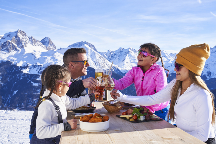 Familienzeit auf der Sonnenterrasse eines Bergrestaurants im Skigebiet Savognin (Foto: © Tourismus Savognin Bivio Albula AG / Christoph Gramann) Familie stösst auf Sonnenterrasse im Skigebiet Savognin an, umgeben von verschneiten Bergen