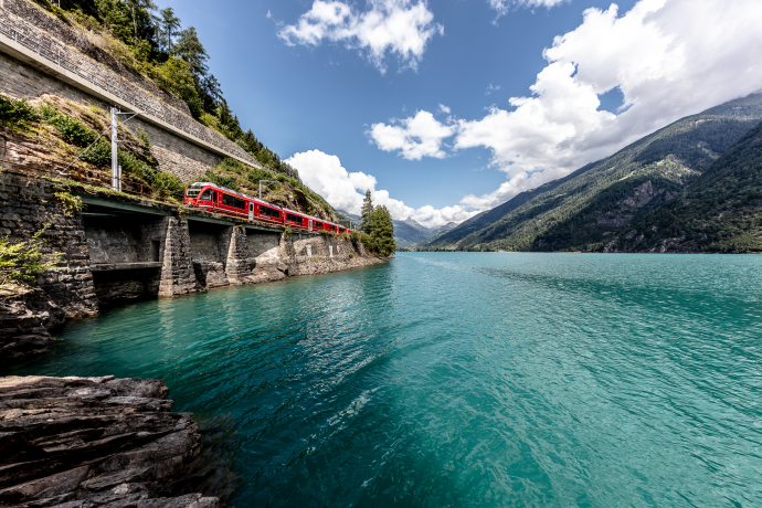 Zwischen Wasser und Bergen: Die Rhätische Bahn folgt dem Ufer des Lago di Poschiavo Richtung Tirano (Foto: © Rhätische Bahn / Andrea Badrutt) Regionalzug der Rhätischen Bahn am Lago di Poschiavo an einem sonnigen Sommertag