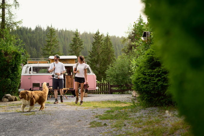 Mit Hund und Wanderschuhen unterwegs – vom TCS Camping Flims starten Touren direkt vor der Tür (Foto: © Nicholas Iliano) Paar mit Hund vor Campervan auf dem TCS Camping Flims