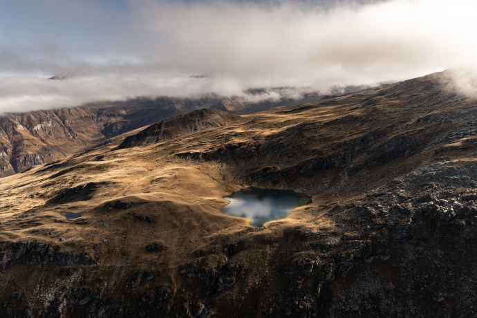 Selvasee (Foto: © Lukas Schweizer) Luftaufnahme eines Bergsees bei Vals, umgeben von Hügeln und Wolken.