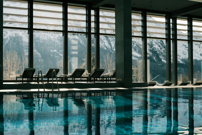Indoor-Pool im Kulm Hotel St. Moritz mit stilvollem Spa-Ambiente (Foto: © Kulm Hotel St. Moritz) Indoor-Pool mit Liegestühlen und Blick durch Panoramafenster auf die umliegende Bergwelt im Kulm Hotel St. Moritz