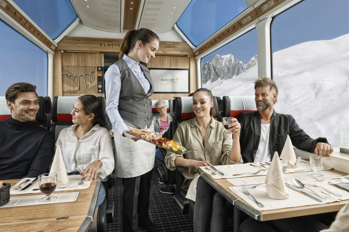 Während der Fahrt mit dem Glacier Express werden frisch zubereitete Gerichte serviert (Foto: © Glacier Express AG / Stefan Schlumpf) Eine Zugbegleiterin serviert im Glacier Express eine kalte Platte