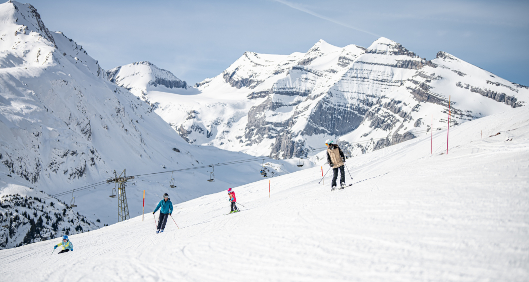 Das Bild zeigt 4 Menschen die mit den Skiern die Piste runter fahren Das Bild zeigt 4 Menschen die mit den Skiern die Piste runter fahren