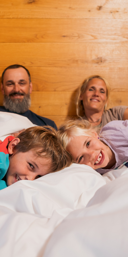 Une famille allongée ensemble sur un lit au rocksresort Laax sourit à la caméra